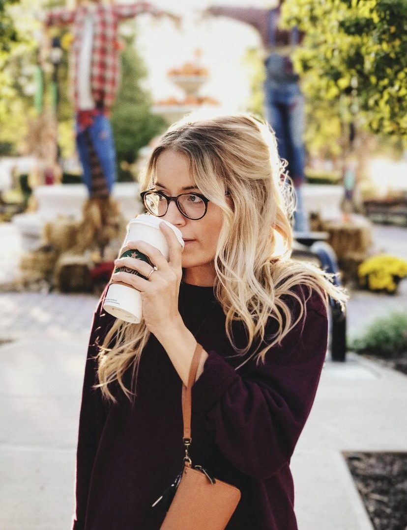Femme dégustant un café dans un parc, elle porte des lunettes, un petit sac au poignet